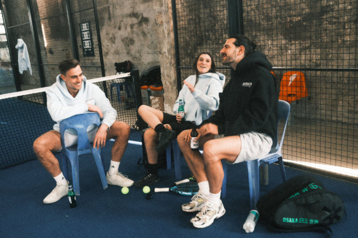 Padel players sitting in a circle on the court wearing BYFOUR Padel clothing